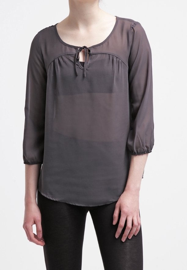 Transparent grå blus med ¾ ärmar, rund halsringning och knytdetalj framtill. Slät textur med lös passform, kombinerad med svarta byxor.