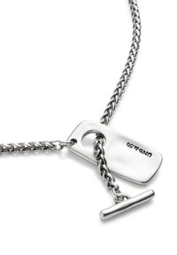 Collier en chaîne en argent présentant une plaque plate gravée et un fermoir à bascule. La chaîne a des maillons entrelacés, offrant une finition texturée.