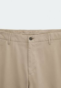 Pantaloni in cotone beige con design a vita piatta, chiusura con bottone e una leggera lucentezza. Presentano passanti per cintura e tasche laterali.