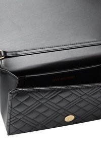 Svart kviltad läderhandväska med en slät yta, guldfärgade detaljer och tryckknappsstängning. Inuti finns ett fack med logotryck.