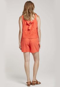 Haut sans manches de couleur corail avec un détail en nœud, des motifs floraux brodés et un ourlet festonné, associé à un short assorti.