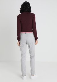 Szare spodnie o wąskim kroju, zaprojektowane z tylnymi kieszeniami. Do nich dobrano bordowy top z długim rękawem. Obuwie to białe trampki.