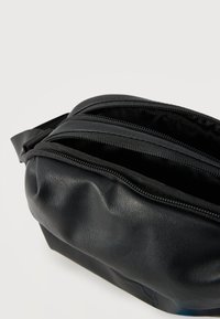 Μαύρο δερμάτινο τσαντάκι μέσης με δύο ανοιχτές θήκες με φερμουάρ και ρυθμιζόμενο λουράκι σε απλό ανοιχτό φόντο.