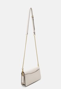 Bolso cruzado en cuero texturizado blanco roto, con una correa de cadena, herrajes dorados y un solapa curva. Dimensiones: compacto y rectangular.
