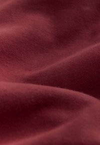Bordeauxfarvet tekstil med en glat struktur, der har let stretch og fint strikket mønster, vist i bløde folder og skygger.
