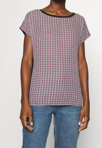 Kortärmad topp i ett mönstrat tyg med röda, vita och blå nyanser, med en svart halsringning och avslappnad passform.