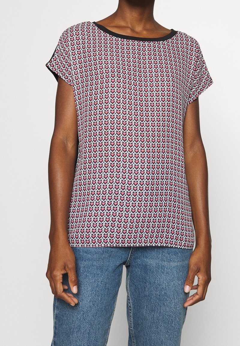 Kortärmad topp i ett mönstrat tyg med röda, vita och blå nyanser, med en svart halsringning och avslappnad passform.