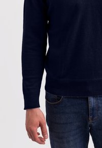 Marinblå stickad tröja med ribbade manschetter och nederkant, parat med mörka denimjeans, som visar en avslappnad passform och mjuk textur.