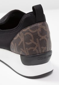 Czarny tenisówka z tekstylną cholewką i brązowym wzorzystym obcasem, z logo Calvin Klein. Biała środkowa podeszwa i czarna gumowa podeszwa zewnętrzna.