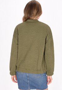 Olivgrön kviltad jacka med blommönster, rund halsringning och elastiska manschetter, matchad med en denimkjol.