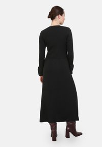 Černé maxi šaty z vroubkované pleteniny s dlouhými rukávy a upnutou sukní. Nosené s kozačkami v barvě vína do kolen. Jednoduchý, jednobarevný design.