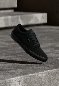 Μαύρα παπούτσια skate με λείο ύφασμα πάνω, επίπεδη σόλα, στρογγυλή μύτη και έξι θηλιές με αντίστοιχες κορδόνια. Απλός σχεδιασμός με λεπτομέρεια λογότυπου.