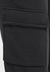 Pantalones cargo negros que presentan un gran bolsillo cargo plano en el lateral, hechos de una tela suave y texturizada con costuras reforzadas.