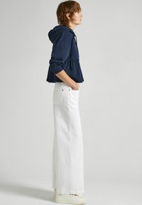 Sudadera con capucha en color marino con diseño peplum, combinada con jeans blancos de pierna ancha y zapatillas ligeras, mostrando un ajuste relajado y un estilo casual.
