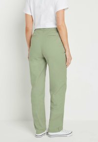 Olijfgroene rechte broek met achterzakken, gemaakt van lichtgewicht stof. Gecombineerd met witte sneakers met zwarte strepen.