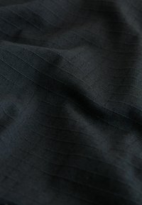 Tissu noir avec des lignes tissées horizontales et verticales discrètes formant un motif en grille texturé et de doux plis.