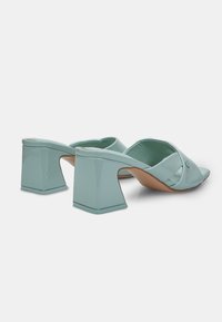 Mint green open-toe mules with a glossy finish, featuring a wide strap and a square heel design. Smooth texture, minimalistic accents.
