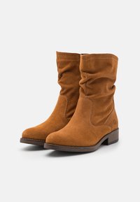 Bottines en suède marron avec un design décontracté, bouts ronds et un faible talon empilé. Présente des coutures visibles et une finition texturée.