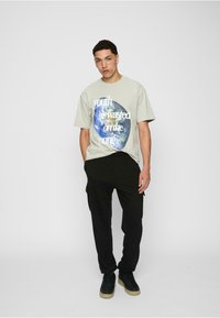 Light green graphic t-shirt with "youth is wasted on the young" text and globe design, paired with black cargo pants and dark sneakers.