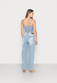 Top ajustado de alças finas em azul claro, com tecido texturizado; combinado com jeans de denim azul claro soltos, apresentando uma bainha desfiada e bolsos.
