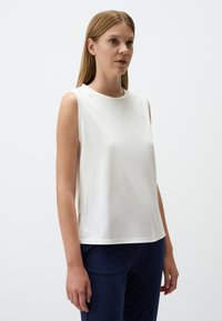 Witte mouwloze top met een ronde halslijn, een gladde textuur en een ontspannen pasvorm, gecombineerd met donkerblauwe broeken.
