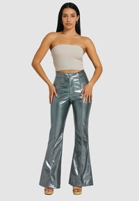 Pantaloni a zampa metallici verdi con cuciture frontali e chiusura a doppio bottone. Abbinati a un top aderente senza maniche di un leggero beige.