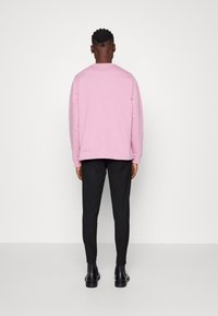 Maglione rosa con maniche lunghe, abbinato a pantaloni neri slim-fit e stivaletti neri alla caviglia. Design minimalista, senza motivi visibili.