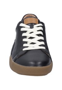 Sneaker in pelle nera con lacci bianchi, un accento in pelle beige sulla linguetta e una suola in gomma marrone testurizzata. Caratteristiche di design minimalista.
