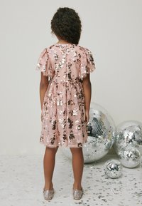 Lyserød pailletkjole med korte puffede ærmer, blomsterdesign og en indsnævret talje. Sæt sammen med glitrende sko og omgivet af disco-kugler.