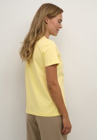 T-shirt en coton jaune à manches courtes avec un col rond, offrant une coupe décontractée et une texture lisse et douce. Accentué par des coutures simples.