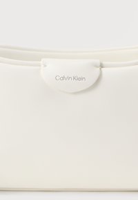 Λευκή τσάντα φάκελος Calvin Klein με λεία, ματ υφή, με στρογγυλεστό κλείσιμο με καπάκι και ανάγλυφη λεπτομέρεια λογότυπου.