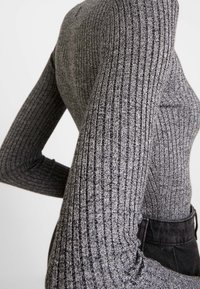 Langsleeve, geribbelde top in donkergrijs met verschillende texturen, slimfit ontwerp en een subtiele glans, gecombineerd met zwarte high-waisted broek.