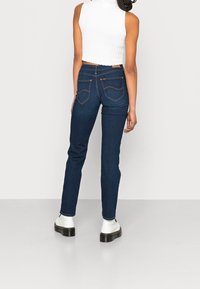Dark blue skinny jeans with a high waist, featuring stitching details on the back pockets and a smooth denim texture. Worn with a white top.