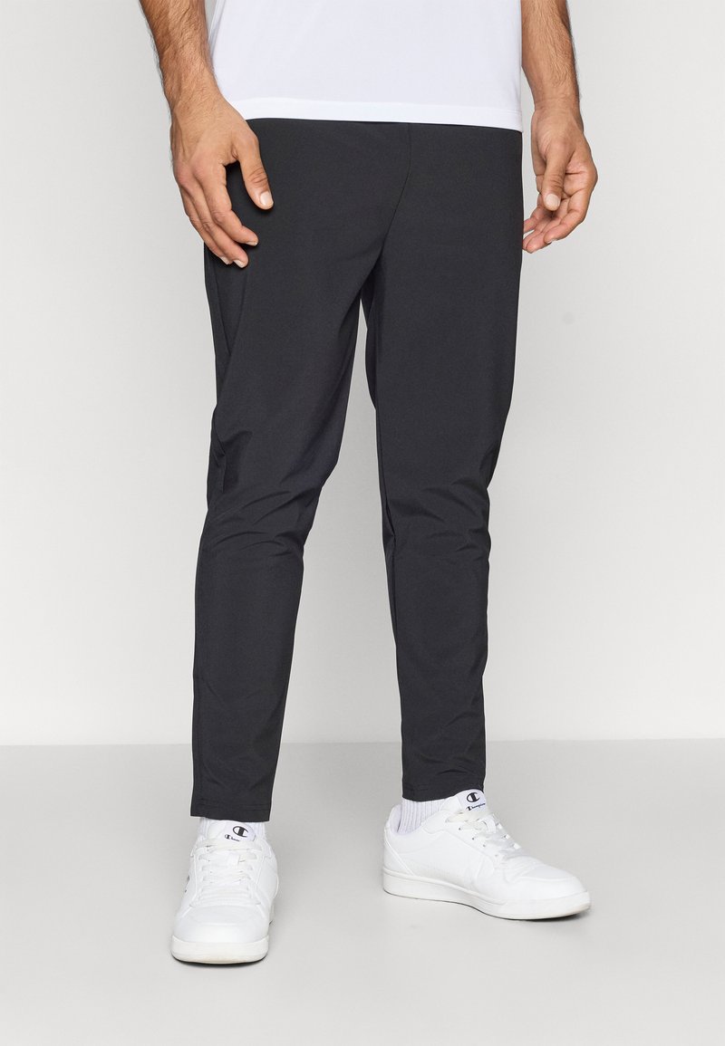 Zwarte slim-fit broek van lichtgewicht materiaal, met een soepele textuur en enkel-lengte snit, gecombineerd met witte sneakers.