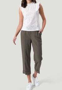 Valkoinen lyhythihainen paita, jossa on reikäkikkauskuvio ja röyhelökoristeet, yhdistettynä väljät oliivinvihreät housut ja valkoiset lenkkarit.