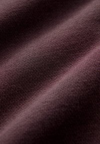 Gros plan d'un tissu tricoté doux de couleur violet foncé montrant une texture fine, étroitement tissée et des plis délicats.
