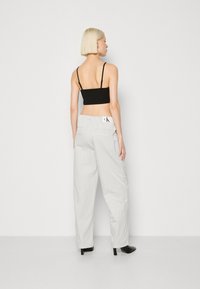 Crop top noir, pantalon large gris clair à rayures verticales, avec une étiquette logo au dos et des chaussures à talons noirs.