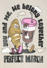 Das Grafische zeigt ein Cartoon-Croissant und eine Kaffeetasse, beide mit Augen und Armen, auf einem grauen Hintergrund. Text: "du und ich, wir gehören zusammen, PERFEKTE PASSUNG."