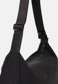 Borsa a spalla nera in nylon con una fascia larga, chiusura con zip e dettagli in pelle, caratterizzata da un logo impresso sulla tracolla e una forma elegante e aerodinamica.