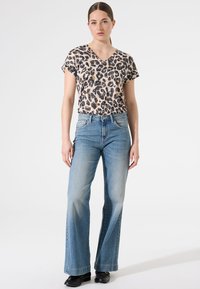 Top de manga corta con escote en V de estampado de leopardo, combinado con unos pantalones vaqueros de pierna ancha en azul claro y zapatos negros. Tejido liso con una textura suave.