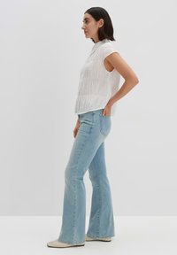 White, textured sleeveless top with a collar, paired with light blue flared jeans. The outfit features a relaxed fit and subtle seams.