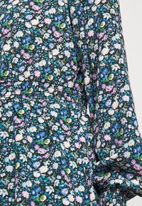 Gros plan sur une robe à manches longues avec un petit imprimé floral bleu, blanc, vert et violet sur fond noir. Détail de la couture à la taille visible.
