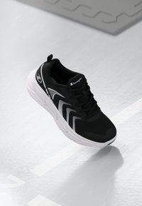 Baskets de sport noires avec une tige en mesh, semelle blanche et motifs rayés subtils sur le côté. Elles disposent d'un col rembourré et de lacets.