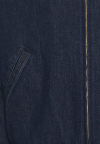 Denimová bunda v tmavě modré barvě, s vysokým límcem, zlatým zipem a boční kapsou s jemnou texturou.