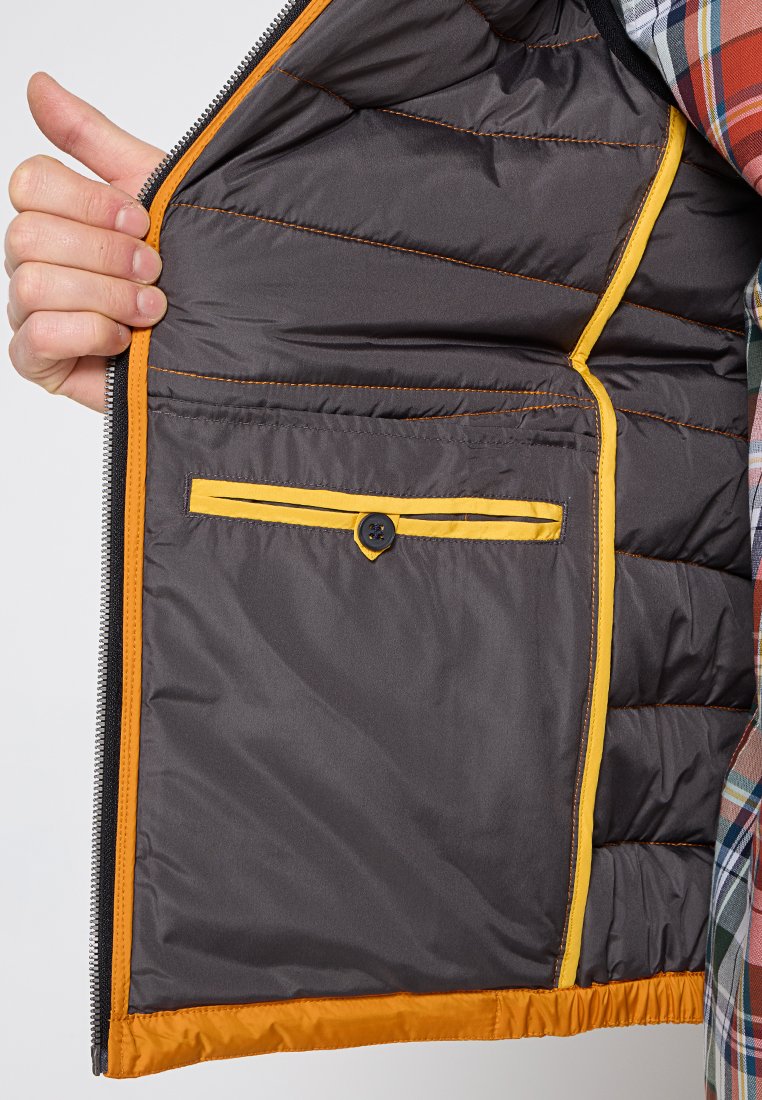 Intérieur d'une veste matelassée grise avec une doublure orange ; présente une poche à boutons avec un contour jaune et une texture matelassée sur les côtés.