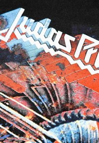 Svart tygtröja med intrikat grafiskt mönster i röd, blå och vit färg. Texten "Judas Priest" i en fet, vinkelräffad stil.