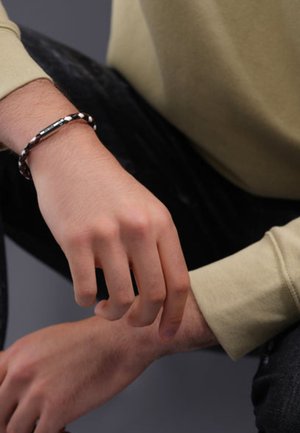 Bruine en zwarte gevlochten leren armband om een pols, met een zilverkleurige metalen accent. De textuur is glad met een gevlochten ontwerp.
