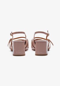Sandales à talons bloc en cuir verni rose avec des brides de cheville. Présentent une texture lisse et un fini brillant, avec une boucle ajustable sécurisée.