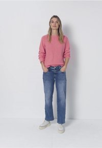 Pull en tricot rose à manches longues, associé à un jean droit bleu clair et des baskets blanches. Design simple, coupe décontractée.