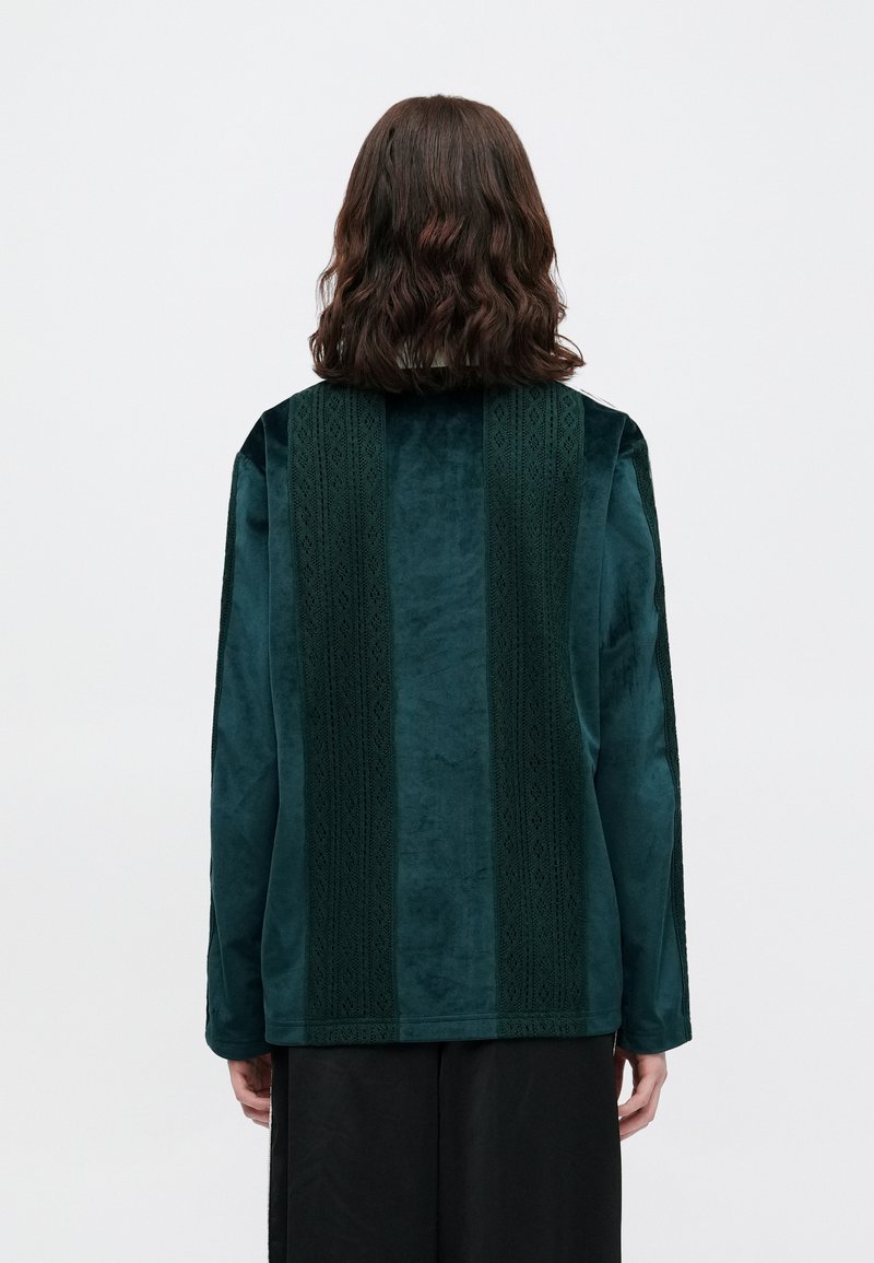 Velvet green jacket featuring textured vertical stripes and long sleeves. Smooth material with intricate detailing along the stripes.